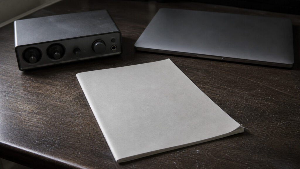 An unmarked booklet beside a closed laptop and a generic audio interface